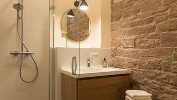 A bathroom with a glass shower enclosure, a wooden vanity with a sink, a mirror, and a stone wall.