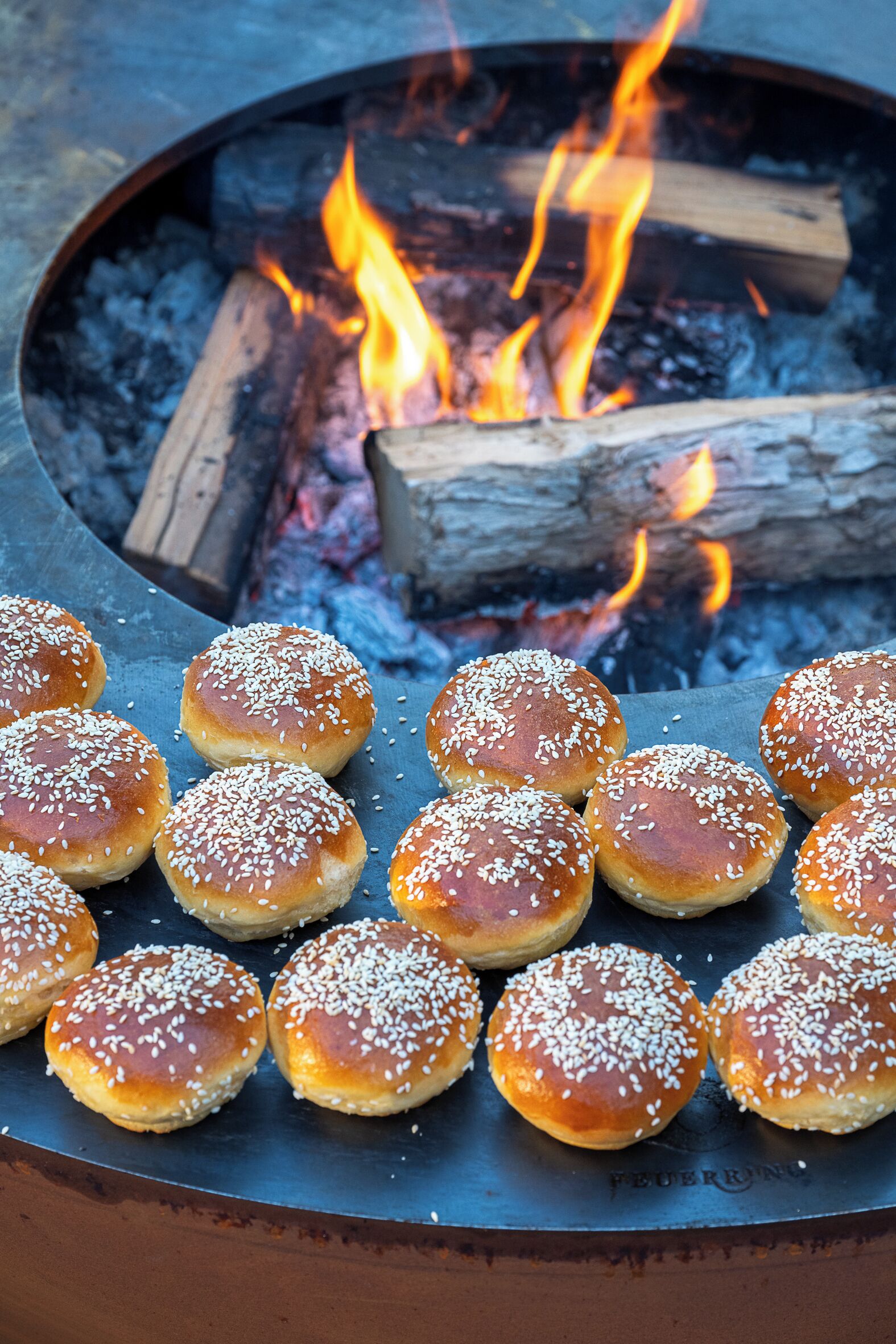 A grill with several buns on it, surrounded by a fire.