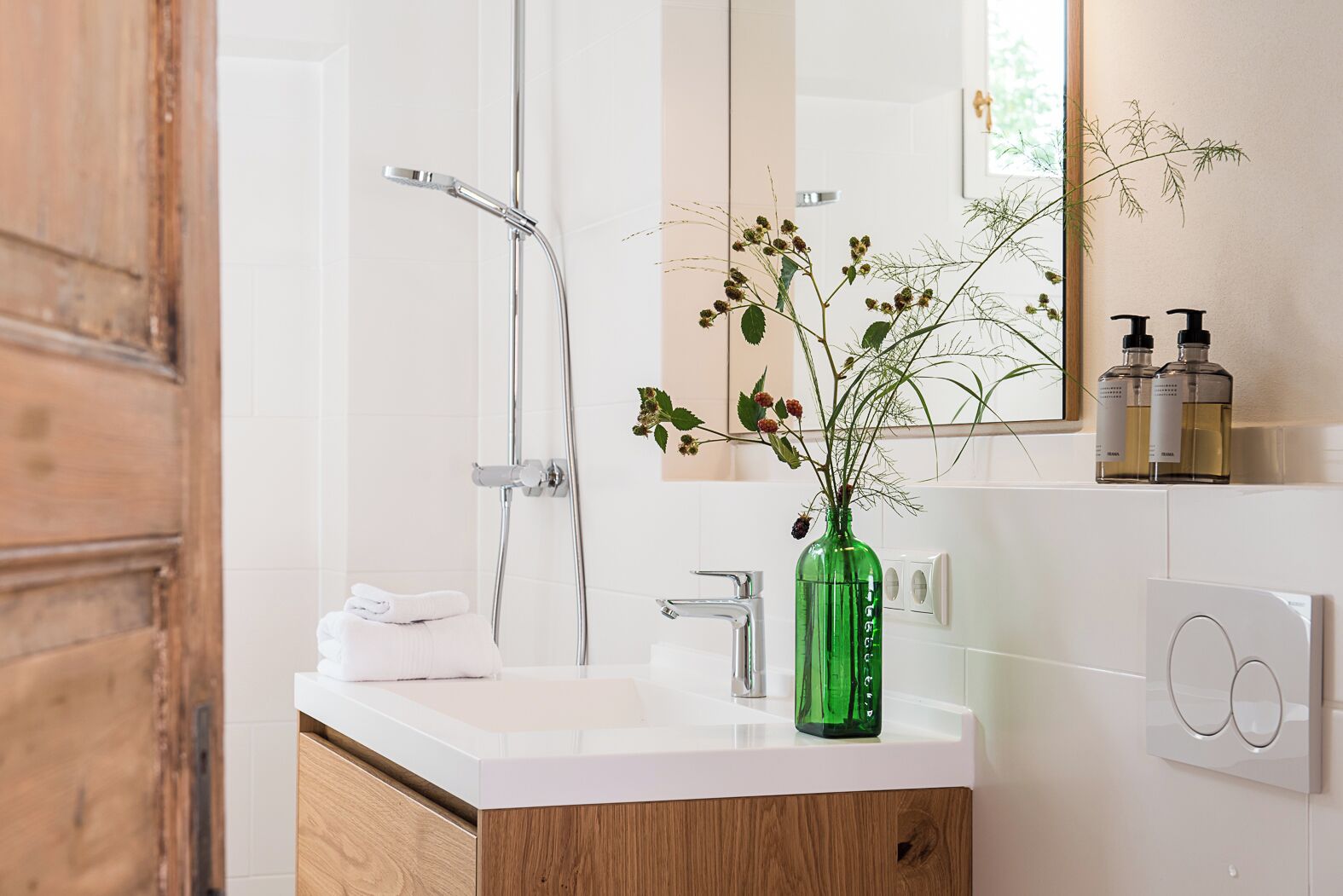 A modern bathroom with a white vanity, a green vase with flowers, and a large mirror.