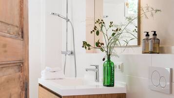 A modern bathroom with a white vanity, a green vase with flowers, and a large mirror.