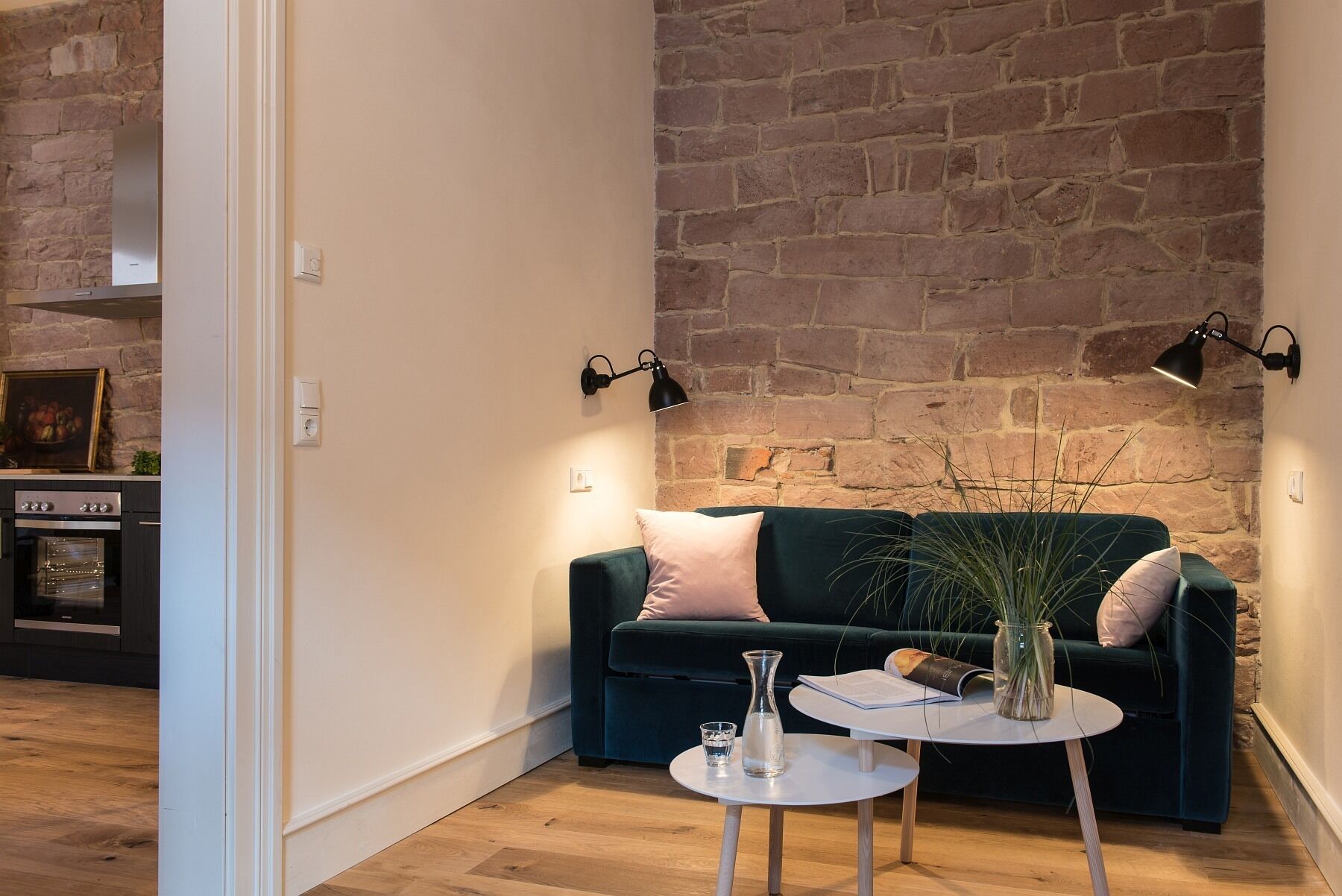 A cozy living room with a dark green sofa, a small white table, and a brick wall.