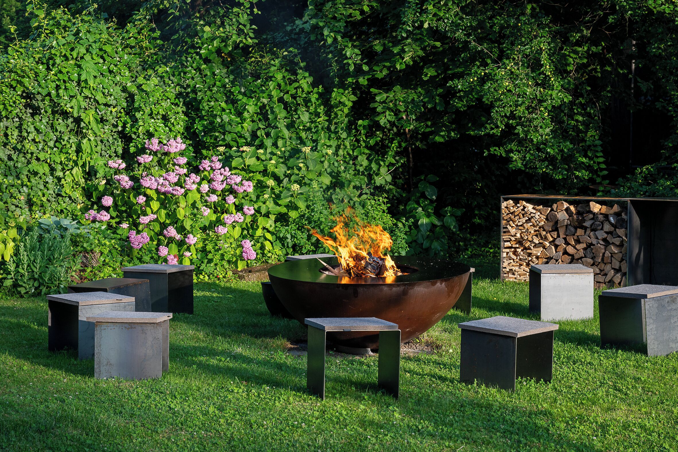 A garden with a central fire feature surrounded by square planters.
