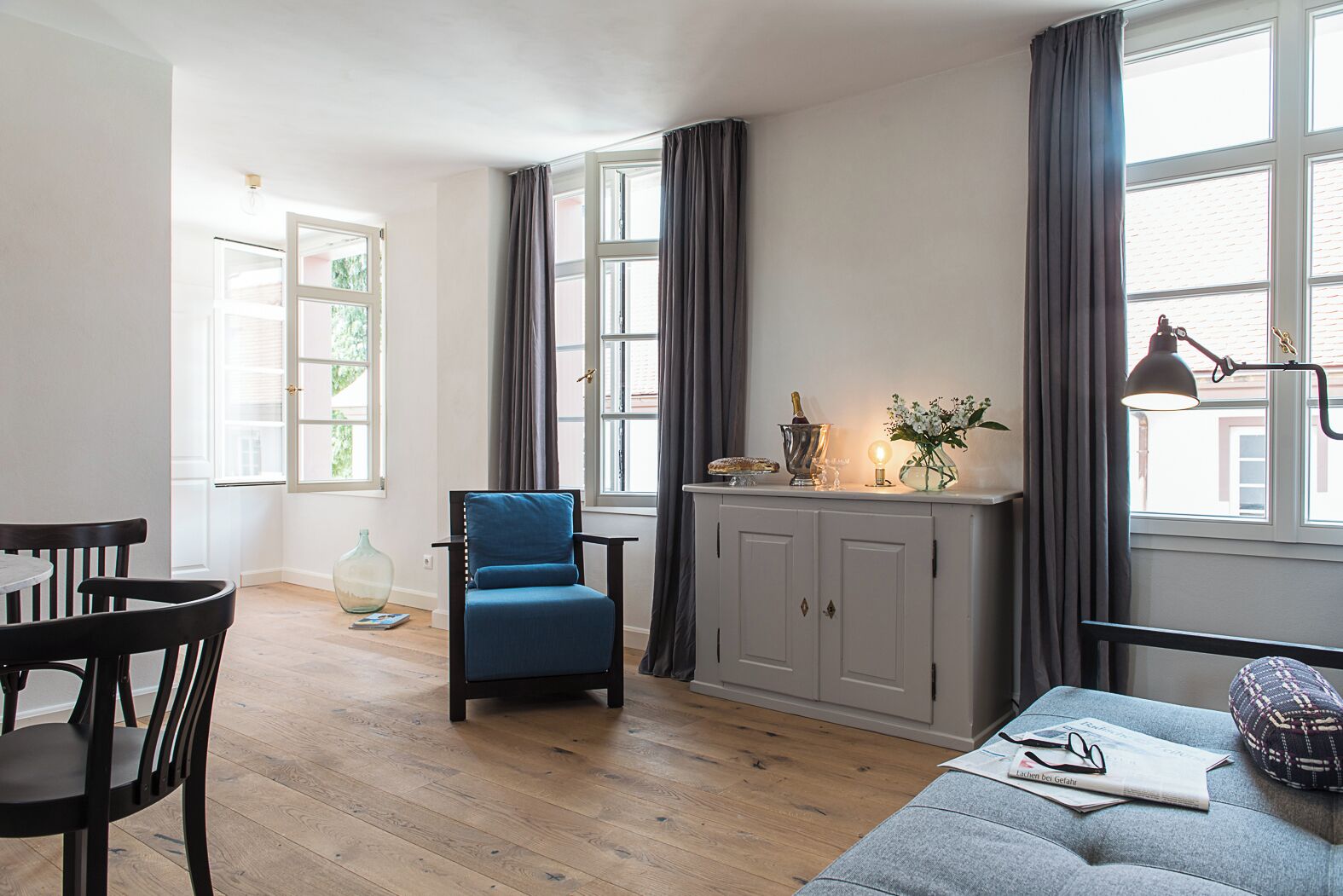 A modern living room with a blue armchair, a grey sofa, and a wooden dining table.