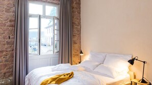 A bedroom with a bed, a nightstand, a lamp, and a window with curtains. - Palais Wunderlich (Lahr)