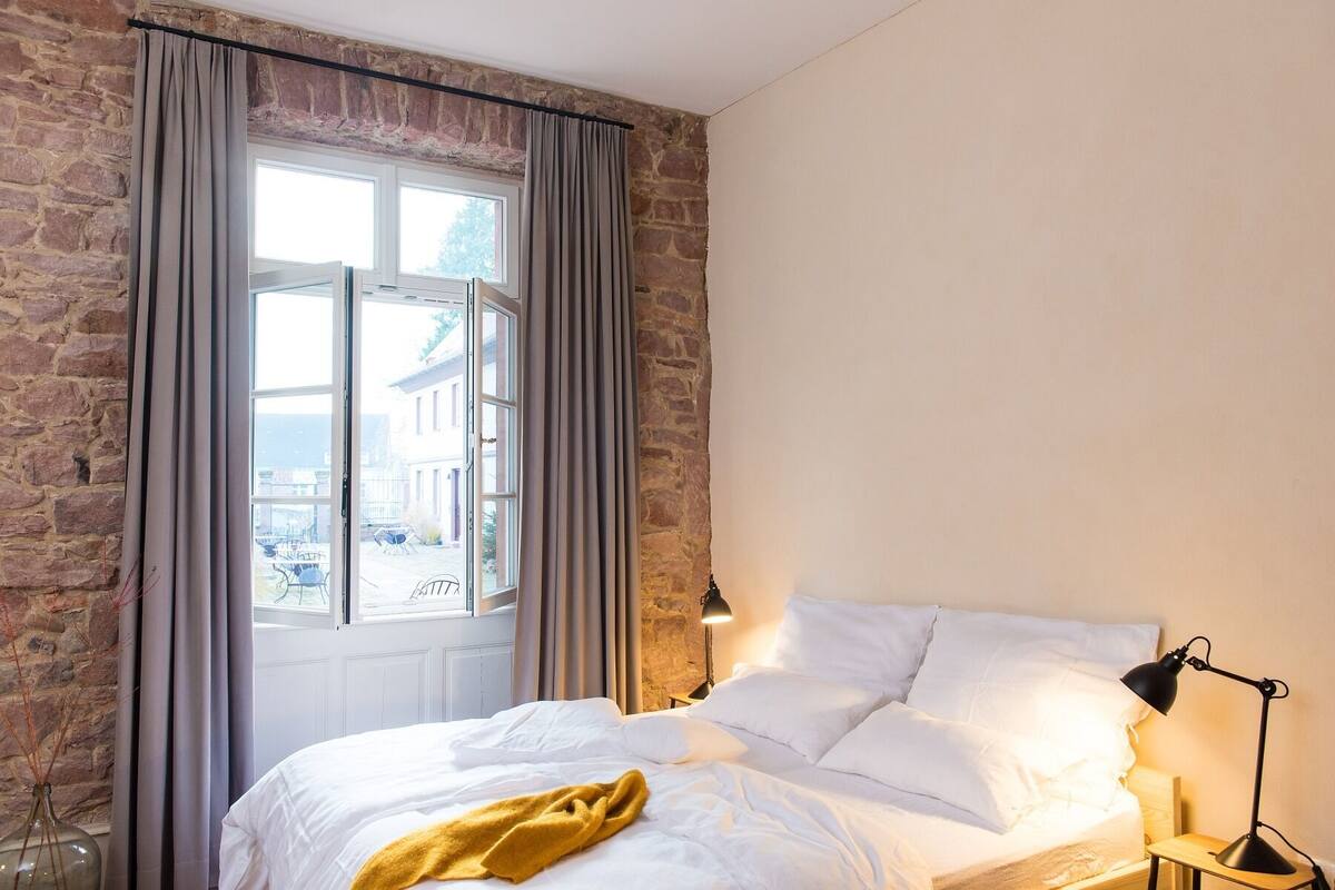 Une chambre à coucher avec un lit, une table de chevet, une lampe et une fenêtre avec des rideaux.