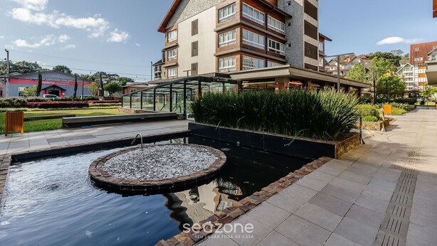 A modern building with a stone facade, a rooftop garden, and a small pond with a fountain. - Beautiful Apart With 2 Bedrooms in Gramado Vdb0201 (Gramado)