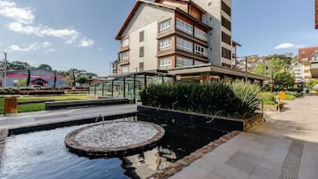 Un edificio moderno con fachada de piedra, un jardín en la azotea y un pequeño estanque con fuente.