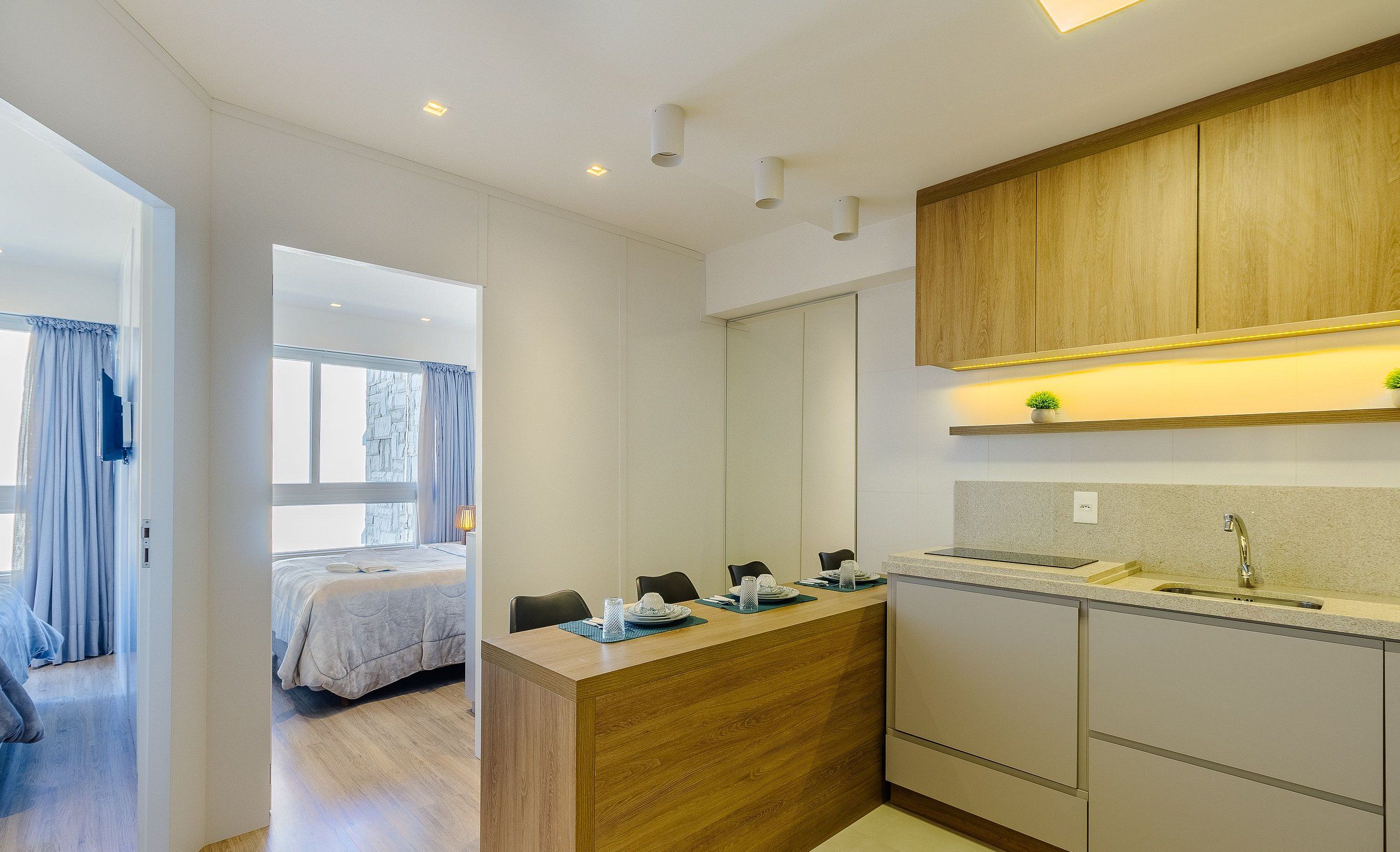 A modern kitchen with wooden cabinets, a countertop, and a sink. There is a dining area with a table and chairs.