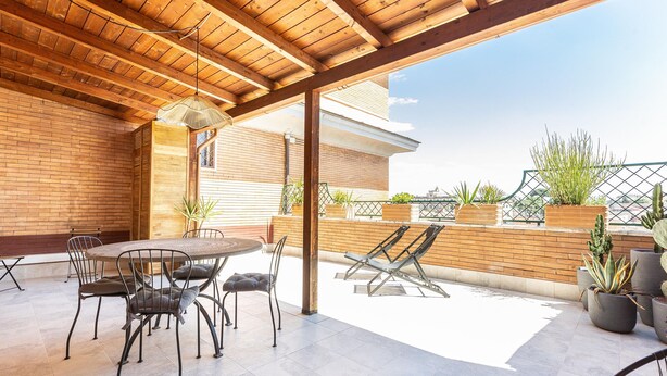 A covered patio with a round table and chairs, potted plants, and a view of the cityscape. - Rental in Rome Constance Terrace Apartment (Rome)