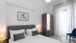 A hotel room with a large bed, a wardrobe, a desk with a lamp, a chair, and a framed picture on the wall. - Rental in Rome Constance Terrace Apartment (Rome)