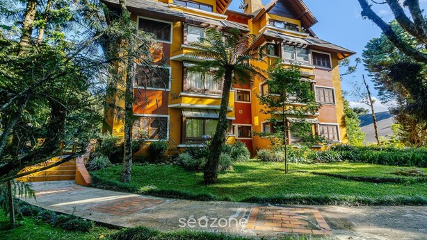 Un edificio de varios pisos con balcones, rodeado de vegetación y un cielo despejado.