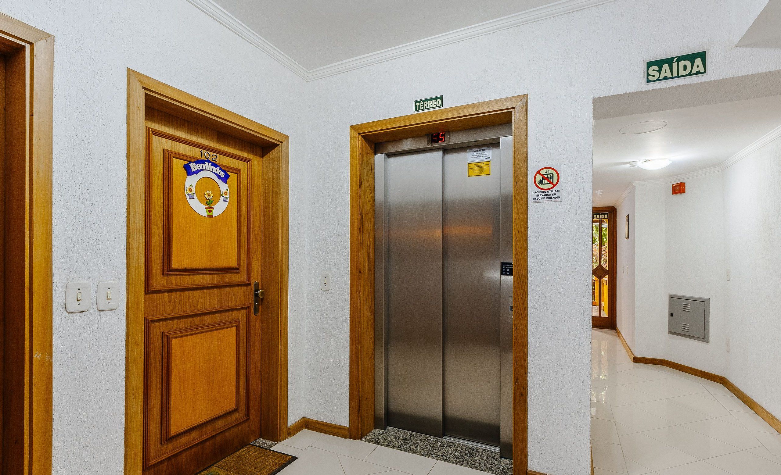 A hallway with a wooden door labeled "Bernardo," an elevator, and a sign indicating the direction to the bathroom.