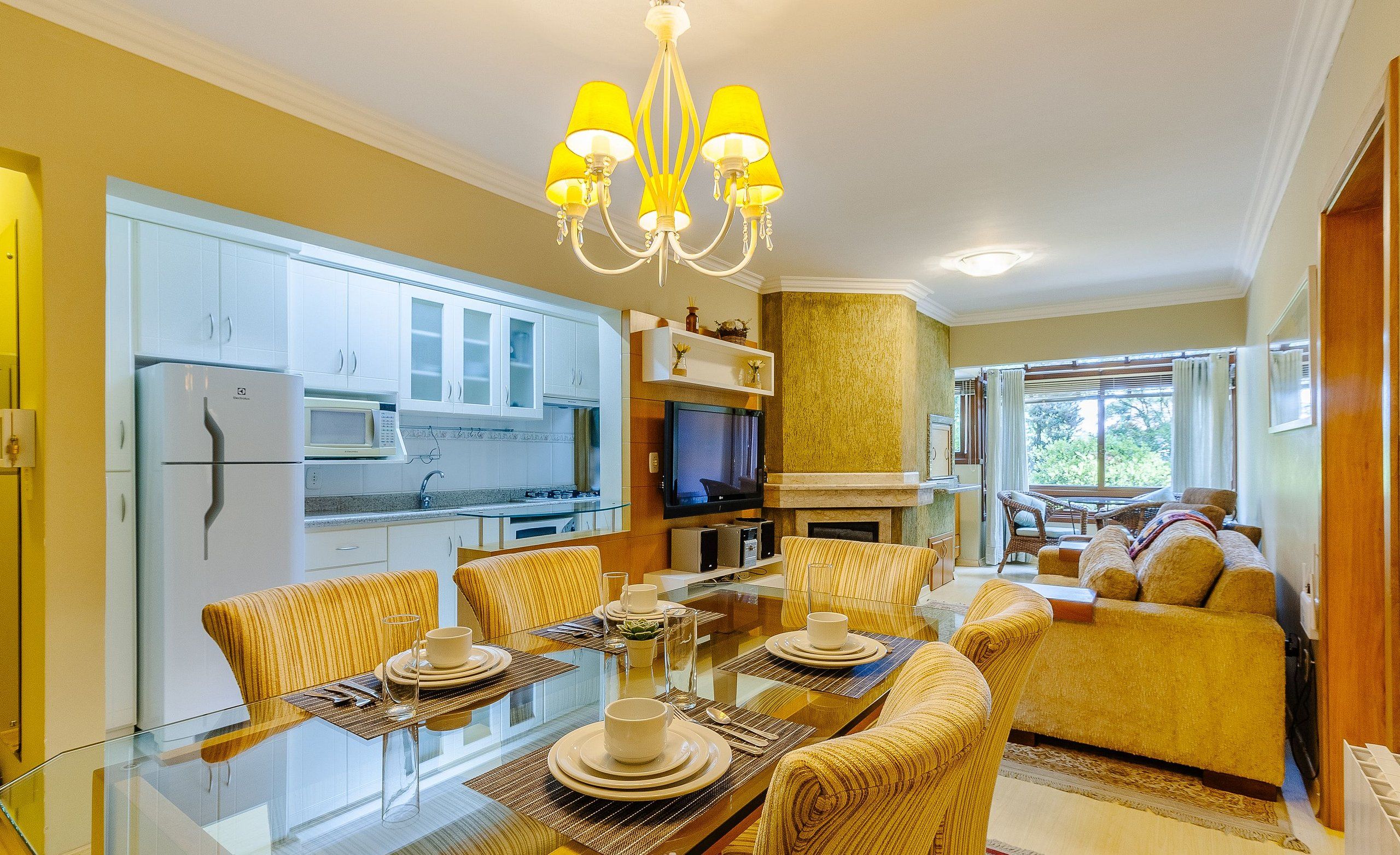 Una sala de estar moderna con una mesa de comedor de vidrio, sillas amarillas, un sofá y un televisor.