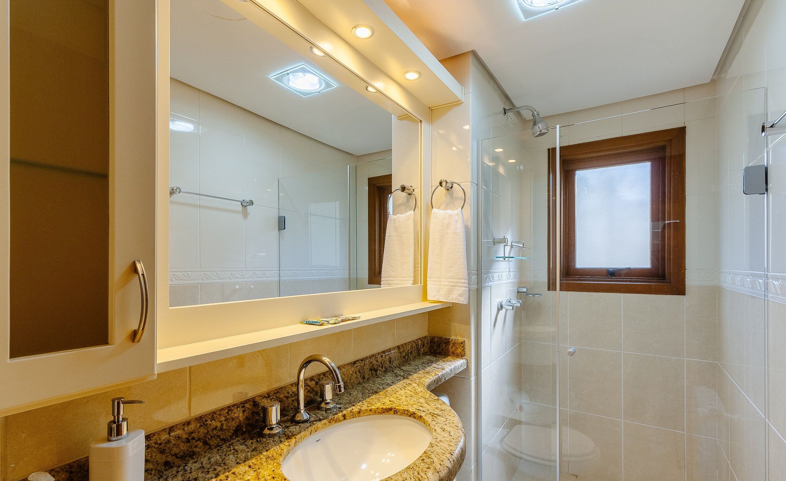 Une salle de bain moderne avec un lavabo surmonté d’un plan de travail en granit, un grand miroir et une cabine de douche en verre.