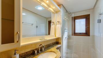 A modern bathroom with a granite countertop sink, a large mirror, and a glass shower enclosure.