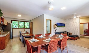 A modern kitchen with a built-in refrigerator, a dining area with a wooden table and orange woven chairs, and a living area with a sofa and a geometric-patterned wall. - Beachfront House in Arraial Dajuda Vva0490 (Porto Seguro)