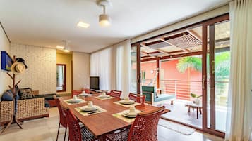 A dining area with a wooden table set for four, surrounded by wicker chairs, with a large sliding glass door leading to an outdoor space.