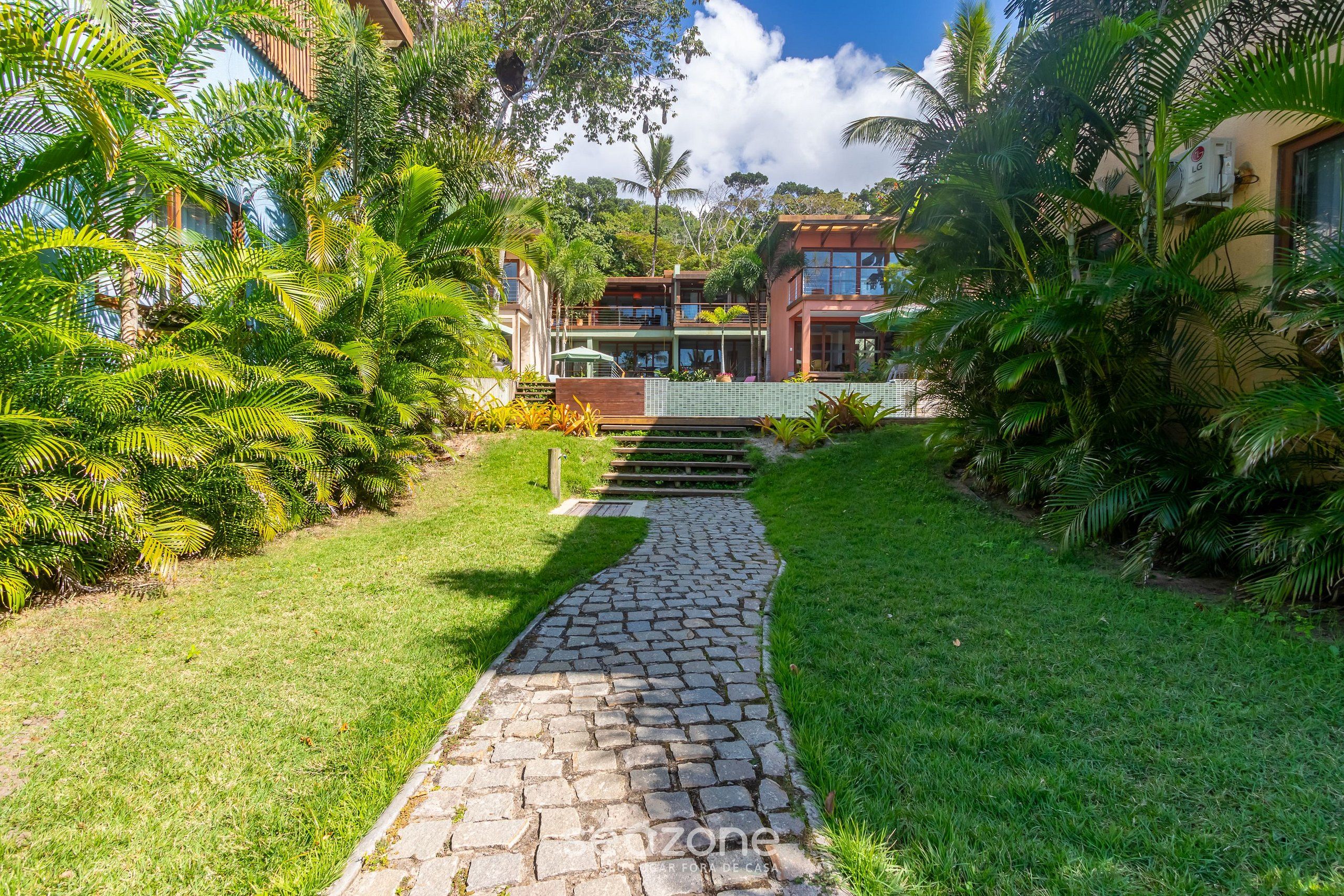 A paved pathway leading to a two-story building surrounded by lush greenery and palm trees.