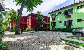 A courtyard with a paved area, a tree, and two buildings with balconies and windows. - Beachfront House in Arraial Dajuda Vva0490 (Porto Seguro)