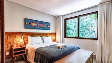 A bedroom with a bed, bedside table, lamp, and a window with a view of greenery.