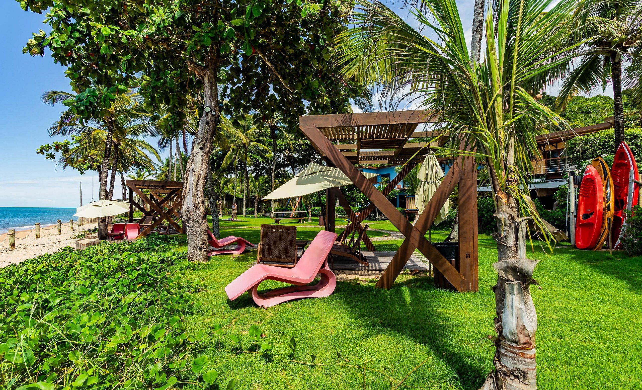 Un resort tropical con vista a la playa, sillas de descanso y una pérgola de madera.