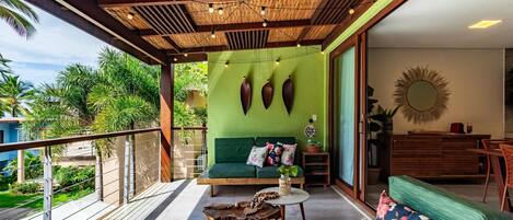 A balcony with a wooden ceiling, a green sofa, a wooden coffee table, and a view of palm trees.
