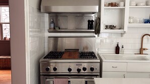 Una cocina con estufa de acero inoxidable, armarios blancos y piso a cuadros.