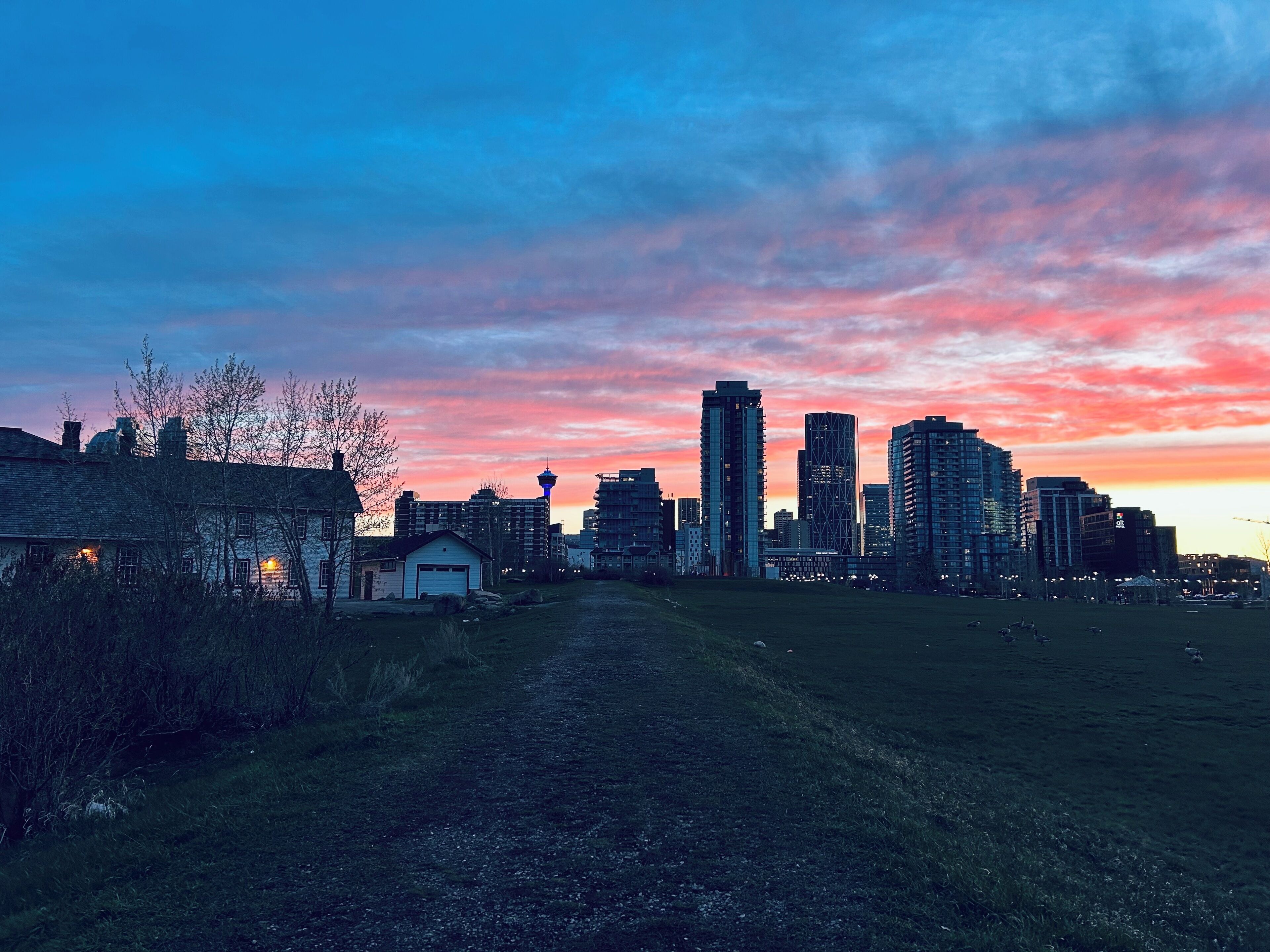 Kaupungin siluetti auringonlaskun aikaan, jossa näkyy moderneja rakennuksia ja kirkas taivas.