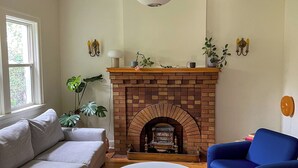 Una sala de estar con chimenea de ladrillo, ventilador de techo blanco, un sillón azul y un sofá blanco.