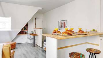 Une cuisine moderne avec un plan de travail en bois, deux tabourets de bar et un coin repas comprenant une chaise et une table.