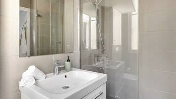 Une salle de bain moderne avec un lavabo blanc, une douche en verre et un grand miroir.
