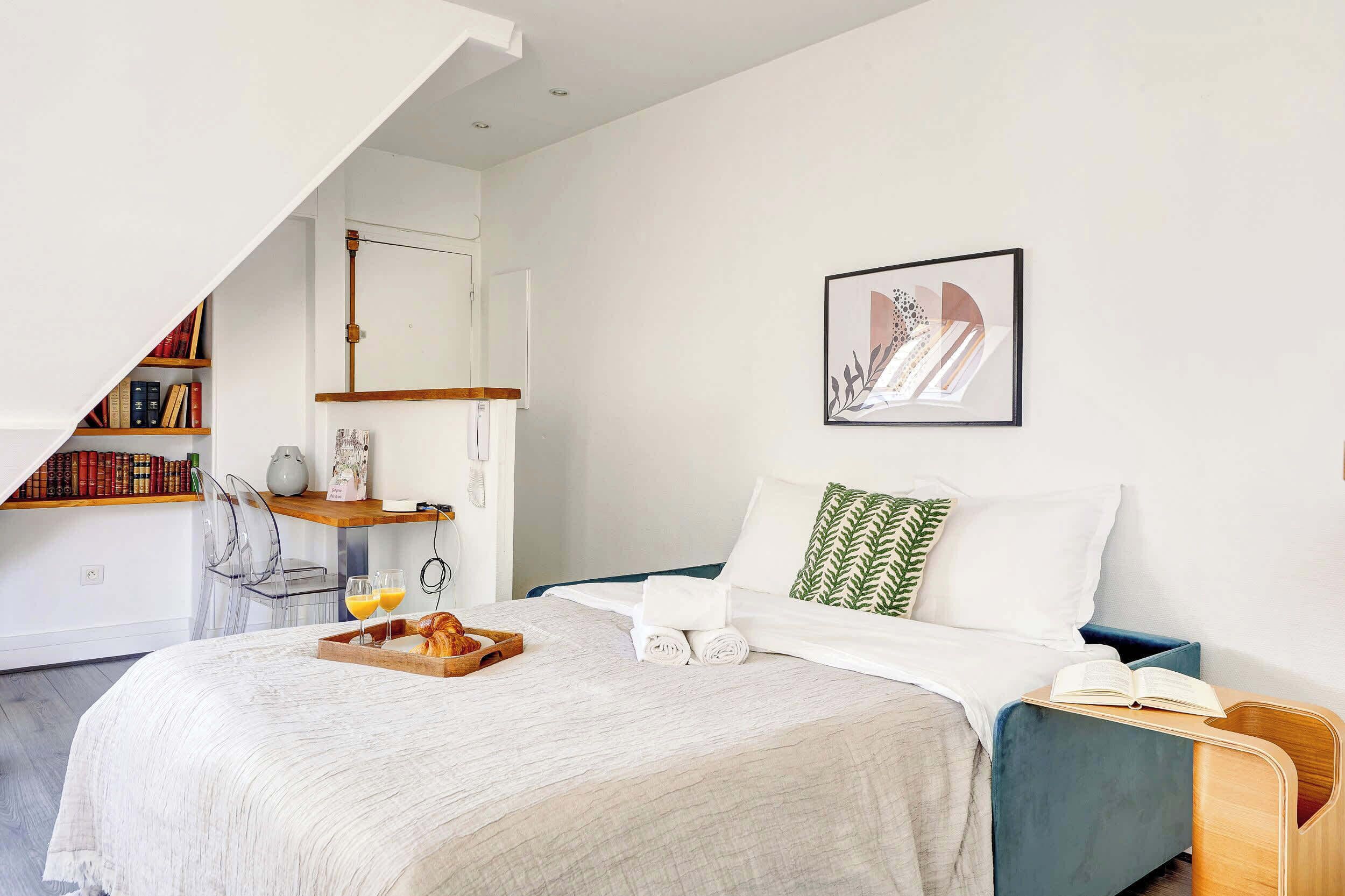 Une chambre à coucher moderne avec un lit, une table de chevet, une bibliothèque et une œuvre d’art encadrée accrochée au mur.
