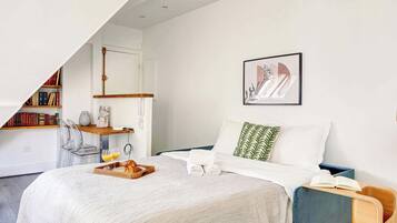Une chambre à coucher moderne avec un lit, une table de chevet, une bibliothèque et une œuvre d’art encadrée accrochée au mur.