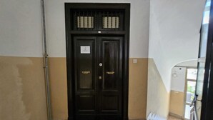 Una puerta de madera oscura con un pequeño ventanal encima, un felpudo con la palabra “WELCOME” y un suelo de baldosas.