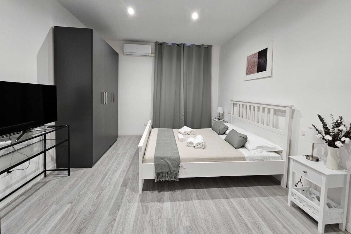 Un dormitorio moderno con cama, televisor, armario y mesita de noche.