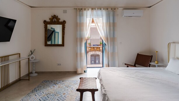 A hotel room with a bed, a small table, a chair, a TV, a mirror, and a view of the outside balcony. - Dolce Vita Central Apartment by Wonderful Italy (Catania)