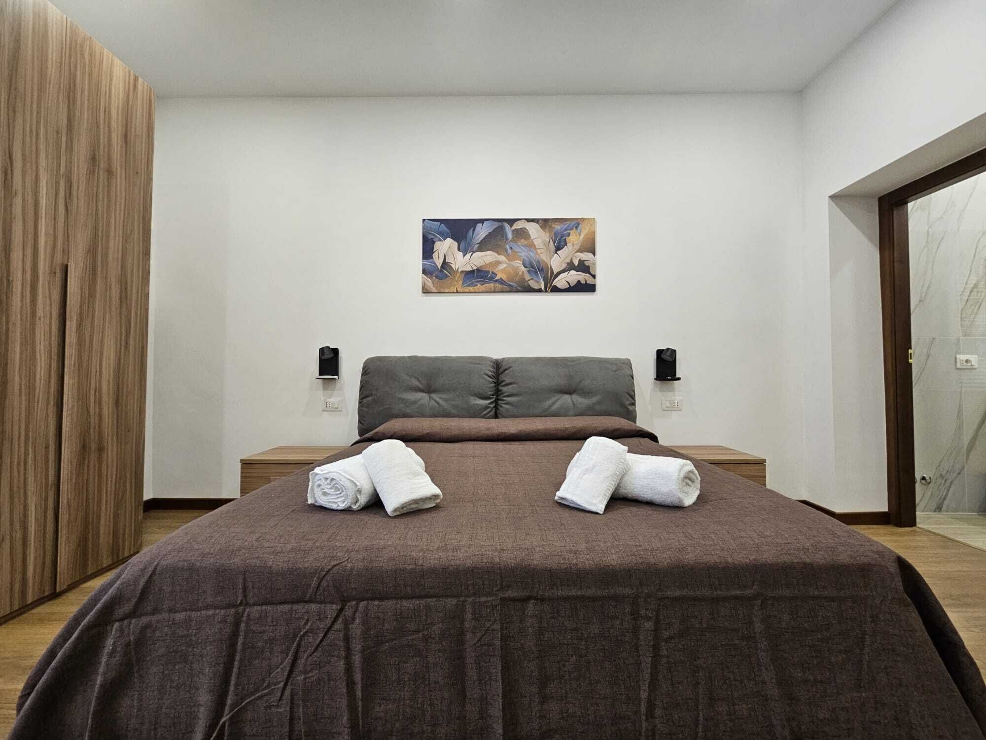 Un dormitorio moderno con una cama grande, dos mesitas de noche, una obra de arte colgada en la pared y un armario de madera.
