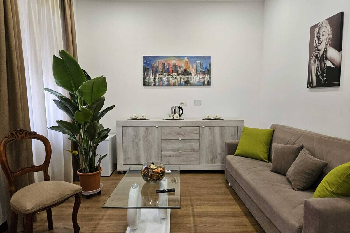 Un salon comprenant un canapé, une table basse en verre, une chaise en bois, une plante en pot, un meuble et un tableau accroché au mur.