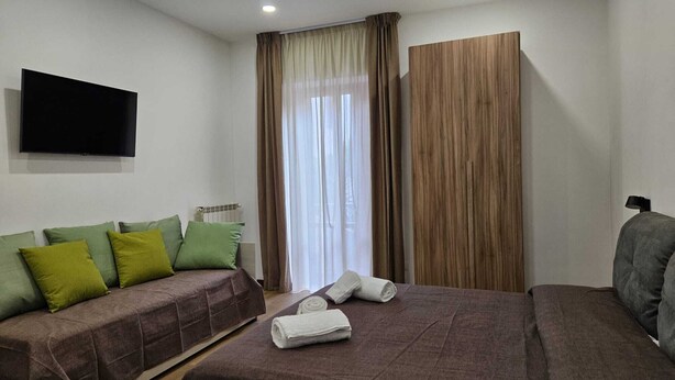 Ein Hotelzimmer mit einem Bett, einer Couch, einem Fernseher und einem Fenster mit Vorhängen.