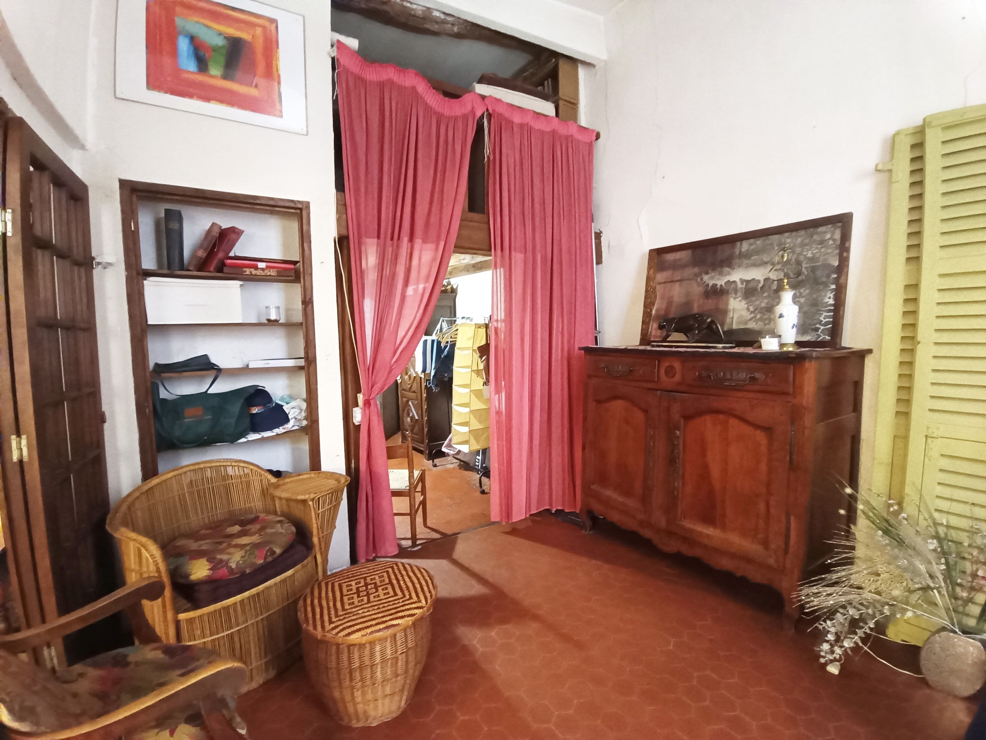 Een kamer met een houten kast, rieten meubels, een televisie en een rood gordijn.