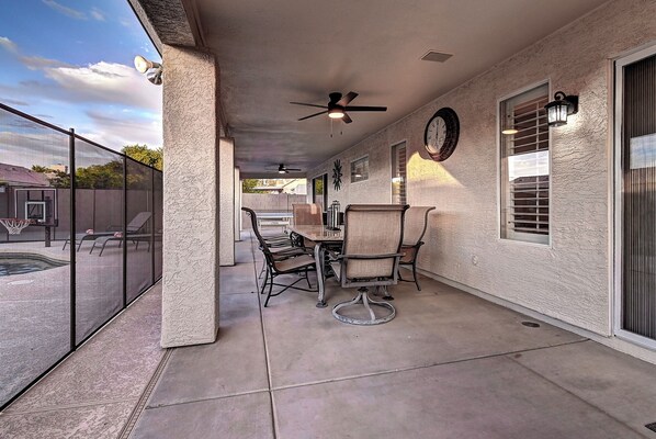 Une terrasse couverte avec une table et des chaises, un ventilateur de plafond et une horloge au mur.