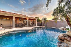 Une piscine avec un espace patio, un coin salon couvert et une vue sur le coucher de soleil.