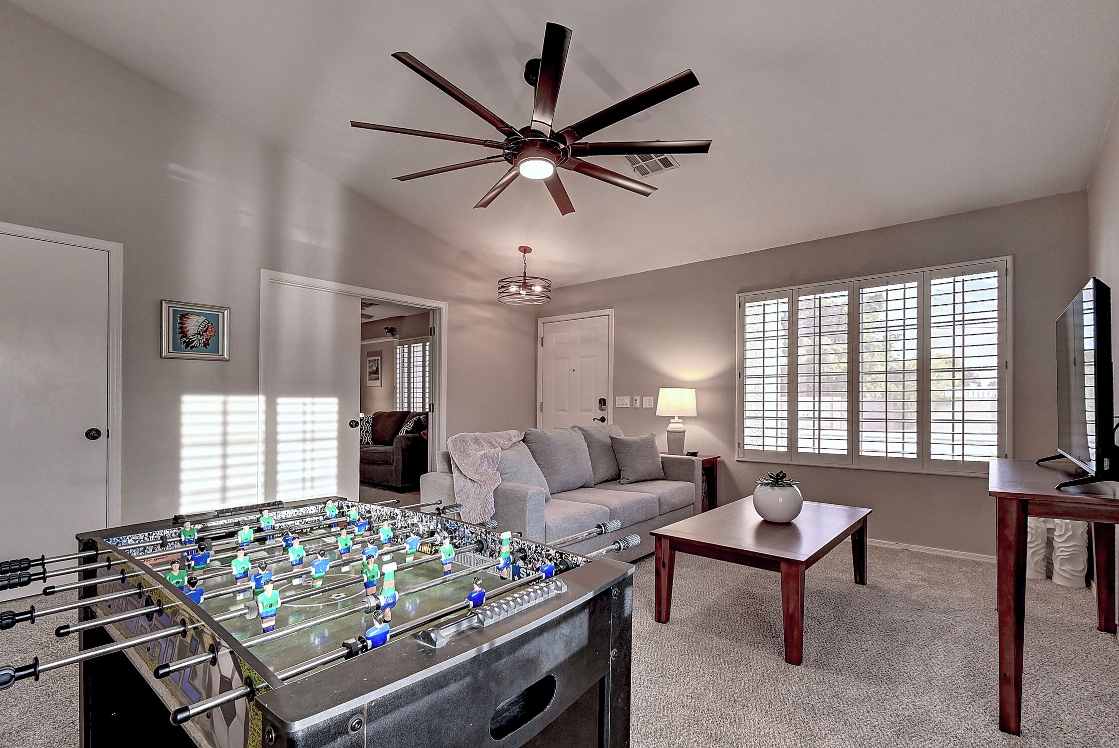 A living room with a foosball table, a ceiling fan, a sofa, a coffee table, and a TV.