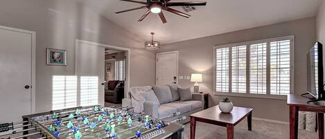 A living room with a foosball table, a ceiling fan, a sofa, a coffee table, and a TV.