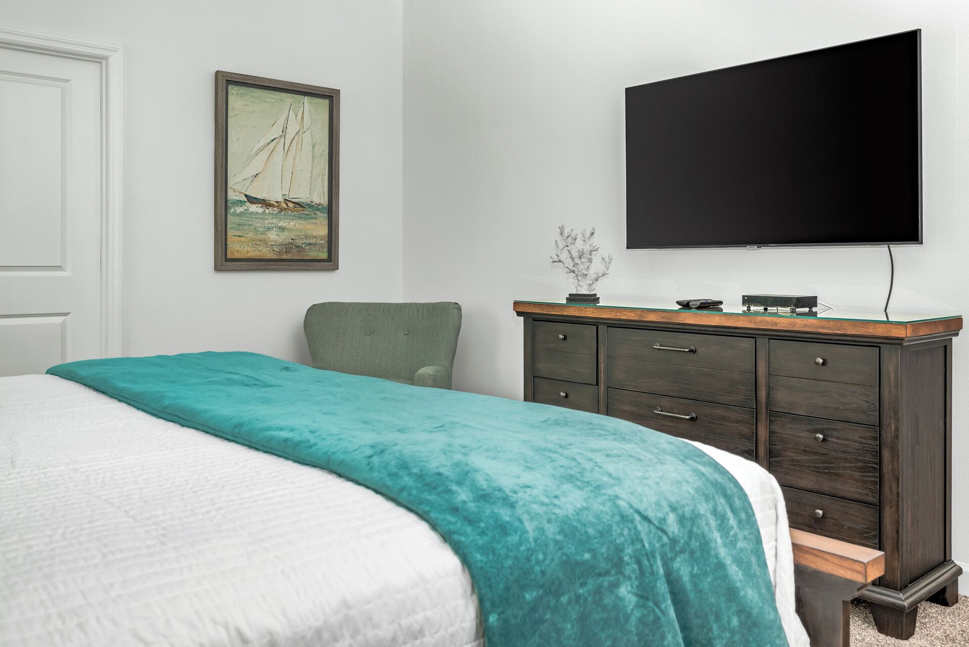 A bedroom with a bed, a dresser, a television, and a painting on the wall.