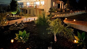 Una casa moderna con un patio amplio, un jardín bien cuidado con diversas plantas y una piscina al fondo.