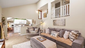 A spacious living room with a grey sofa set, a coffee table, and a kitchen in the background.