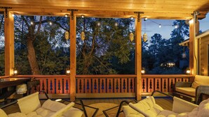 An outdoor deck with wicker chairs and a wooden railing, overlooking a forested area.