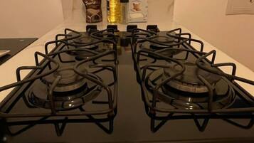 A kitchen with a black stove top, a bottle of cooking oil, a bag of flour, and a box of salt on the counter.