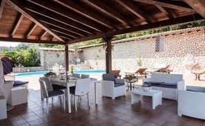 A covered outdoor patio with white wicker furniture, a pool, and stone walls. - Villa Blondie in Castellammare del Golfo (Castellammare del Golfo)